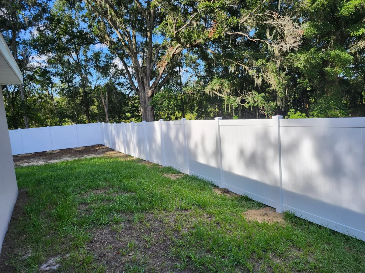 White vinyl privacy fence wrapping backyard with pool cage view — Ocala FL